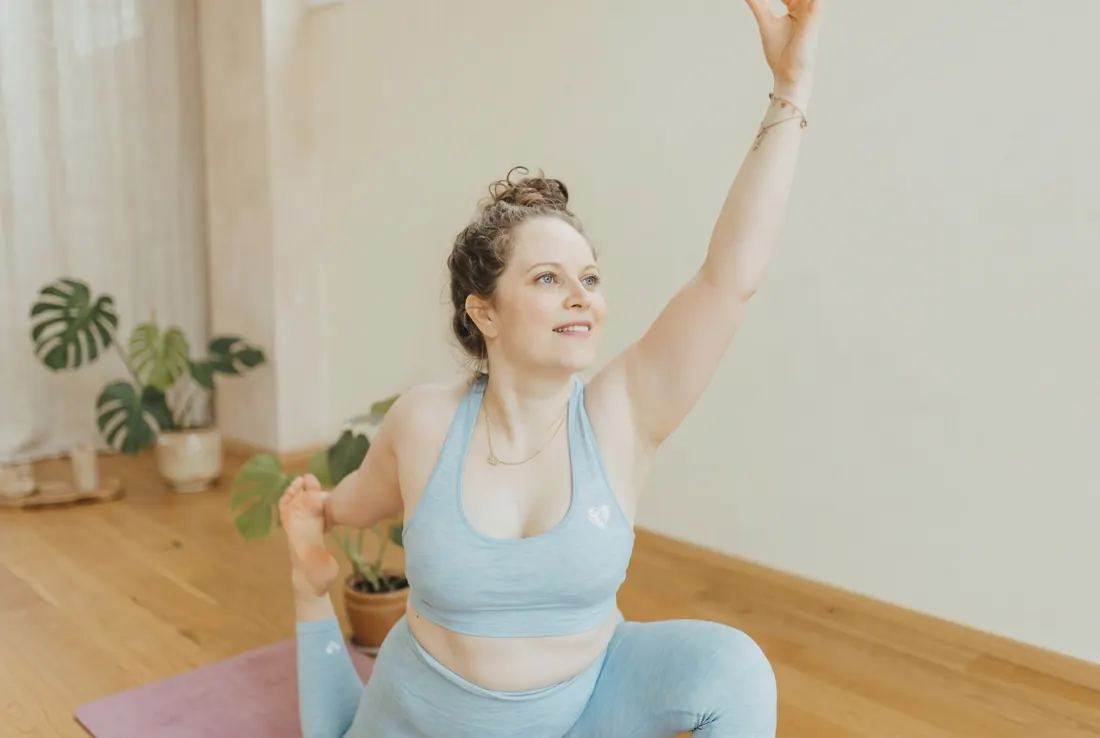 Frau streckt in einem hellen Kursraum einen Arm nach oben, Hatha Yoga